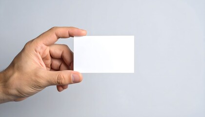 A person's hand holds a blank white business card against a light gray background.