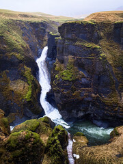 Steep mossy walls of Fjadrargljufur gorge frame the winding Fjadra river in south Iceland beneath a soft gray sky