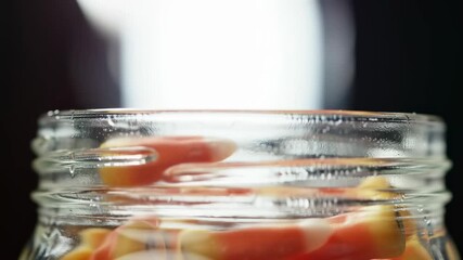 Close up of candy corn falling into a clear glass jar in slow motion - Powered by Adobe