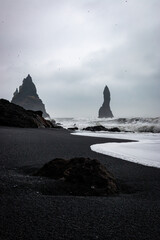 Scenic view of Reynisfjara black sand beach with crashing waves and Reynisdrangar basalt sea stacks...