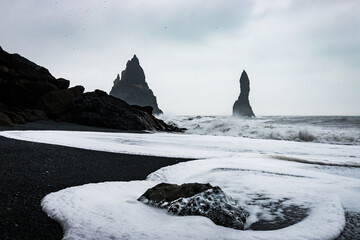 Scenic view of Reynisfjara black sand beach with crashing waves and Reynisdrangar basalt sea stacks in the background near Vik, Iceland