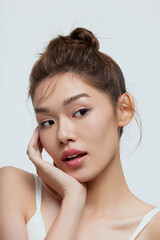 Young woman posing with a hand on her face, showcasing beauty and makeup.