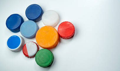 A collection of multicolored plastic bottle caps is arranged on a white surface, showcasing a variety of sizes and colors in a flat-lay style.