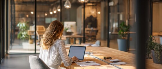 The modern office environment showcasing a woman working on her laptop at a wooden desk.