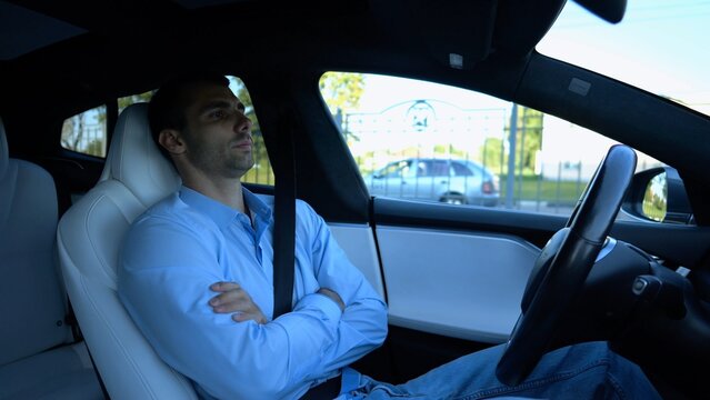 Male businessperson experience to ride an autonomous self driving electric car at urban road. Confident businessman resting during riding on electrical auto with autopilot at city. Slow motion
