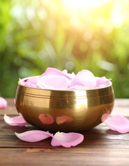 Golden bowl filled with rose petals, blurred nature background