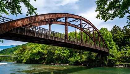 Fototapeta premium Rustic arch bridge spanning a river in a lush green valley.