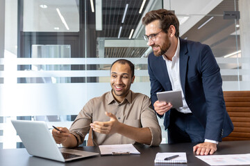 Two colleagues collaborating over a laptop in an office environment
