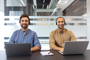 Smiling customer support representatives working on laptops in a modern office environment