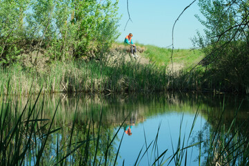 A girl sits on a high lakeshore in spring, gazing thoughtfully into the water.
