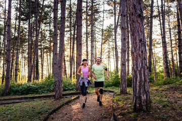 Obraz premium Smiling couple running on a park trail, wearing sportswear and enjoying outdoor fitness and a healthy lifestyle on a sunny day