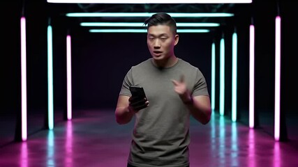 Young Asian Man Presenting Smartphone in Futuristic Neon-Lit Corridor with Reflective Floor - Powered by Adobe