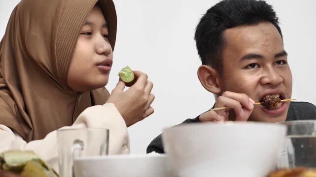Asian muslim siblings doing chit chat talks while eating dinner, sitting on floor with low dining table