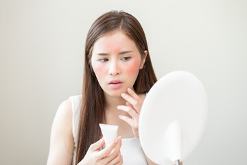 Dermatology, asian young woman looking at mirror, holding cream tube in hand, expression worry and...