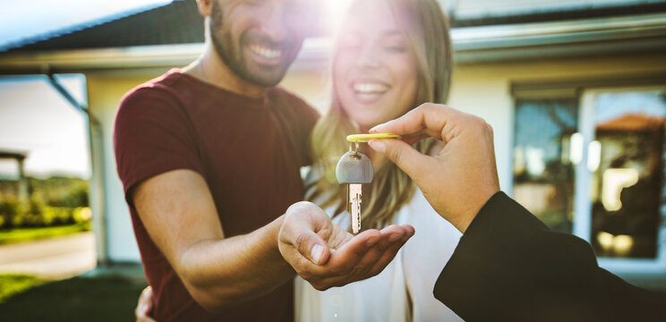 Happy millennial couple receiving keys from realtor, purchasing real estate - Family meeting with real estate agent - New house and real estate concept