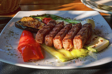 Balkan cuisine. Cevapi - grilled dish of minced meat - with vegetables on rustic table on sunny day