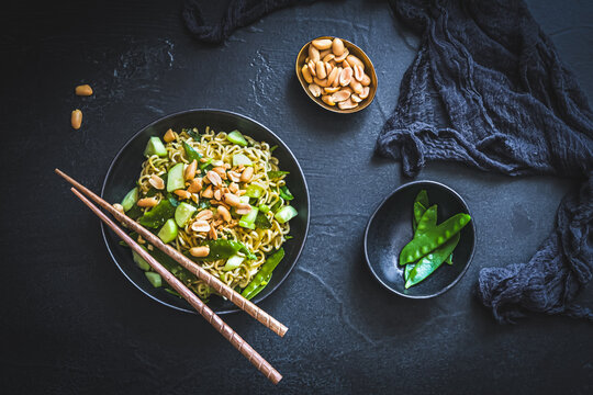 Asian mie noodles with spring onions and sugar peas, topped with cucumber and roasted peanuts