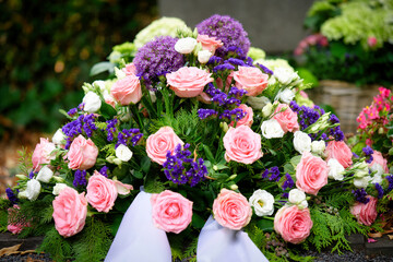 A beautiful and detailed close-up of a funeral wreath, featuring an elegant mix of pink roses, vibrant purple allium, and delicate white blossoms