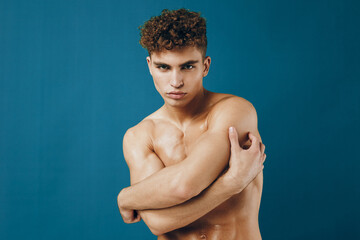 Confident young man posing shirtless against a solid blue backdrop, showcasing strength and...