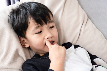 Asian boy biting his nails at home, showing signs of childhood anxiety, stress, emotional problems,...