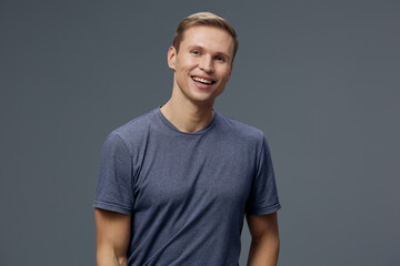 Smiling young man with short light brown hair wearing casual blue t-shirt looking at camera...