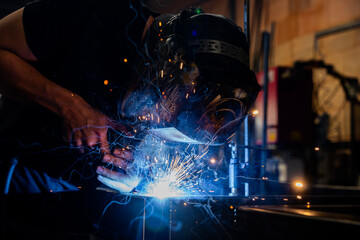 Métallier en plein travail de soudure sur son établi dans l’atelier, étincelles visibles.