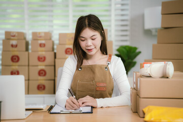A young Asian entrepreneur happily works in her office, managing online retail orders and shipping...
