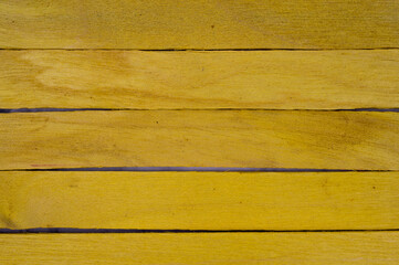 Horizontal arrangement of yellow wooden craft sticks forming a textured, slightly spaced layout...