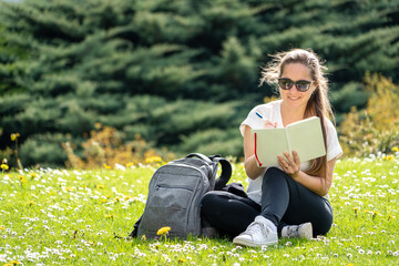Mujer feliz tomando notas en su diario en una hermosa pradera de cesped verdes y flores blancas