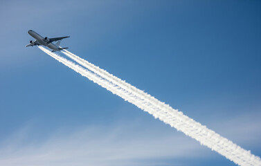 青空を一直線に飛ぶ飛行機と、長く伸びる飛行機雲