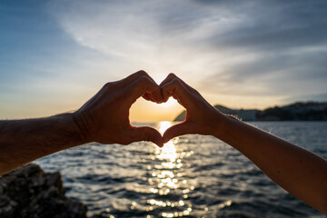 Pareja de enamorados juntando sus manos en forma de corazón en el mar al atardecer