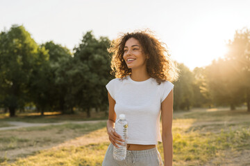 joyful woman holding water bottle looks towards horizon under sun