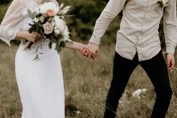 Romantic couple holding hands in meadow at rustic outdoor wedding