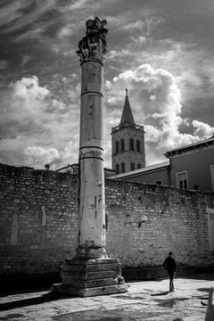 Postal en blanco y negro de la ciudad de Zadar, con la columna romana de la verguenza y un caminante anonimo