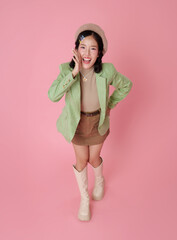 Cheerful Asian woman in green blazer and beret posing playfully on pink background symbolizing...