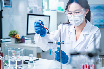 Scientist in protective gear using a pipette to transfer red liquid into a test tube, representing...