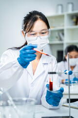 Scientist in protective gear using a pipette to transfer red liquid into a test tube, representing...