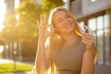 Smiling woman holding orthodontic aligners with hand gesture in sunlight