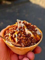 Delicious ice cream sundae with chocolate balls and caramel sauce in hand held cone