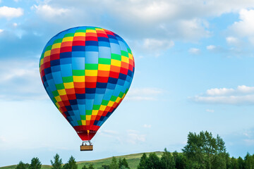 Colorful hot air balloon flying over the green hills and trees at sunset.