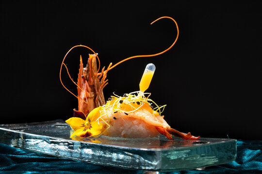 High-end nigiri sushi with a fresh shrimp, artistically decorated with microgreens, edible flowers, and a pipette of sauce.