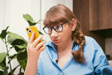 Serious elderly woman talking on smartphone and makes notes in notebook in stylish modern flat