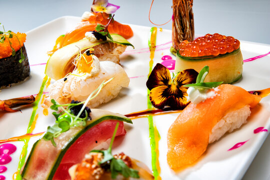 Gourmet sushi and sashimi assortment on a white plate, beautifully styled with edible flowers, colorful sauces and fresh microgreens.