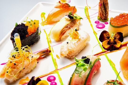 Gourmet sushi and sashimi assortment on a white plate, beautifully styled with edible flowers, colorful sauces and fresh microgreens.