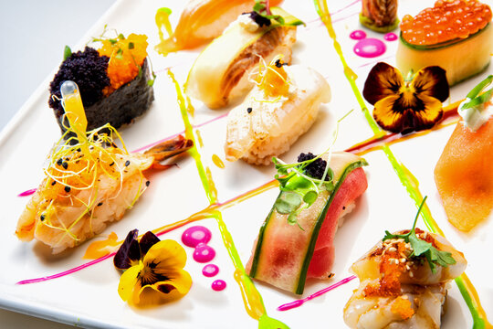 Gourmet sushi and sashimi assortment on a white plate, beautifully styled with edible flowers, colorful sauces and fresh microgreens.