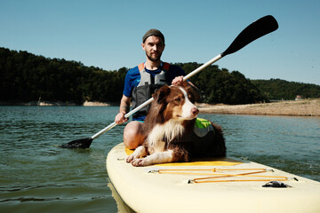 A man paddling on a SUP board with his Australian shepherd dog lying on the board. Relaxing summer...