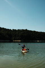 Man paddling on a SUP board with his German Shepherd dog wearing a bright life vest. Summer outdoor...