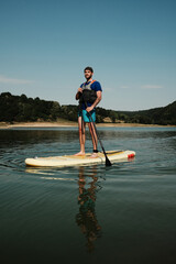 Man standing on paddleboard holding a paddle on calm lake at sunset. Summer outdoor activities on...