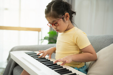 Young girl in yellow shirt playing keyboard indoors with focused expression, learning music at...