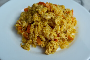 A vibrant, close-up shot of a plate of Plov, a traditional Central Asian rice pilaf. The dish is presented on a clean white plate with a marble background, focusing on the texture and golden-yellow 